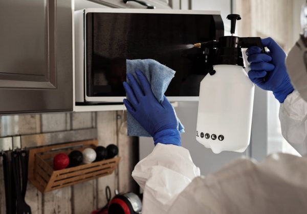 Cleaner disinfecting a kitchen appliance with spray and cloth